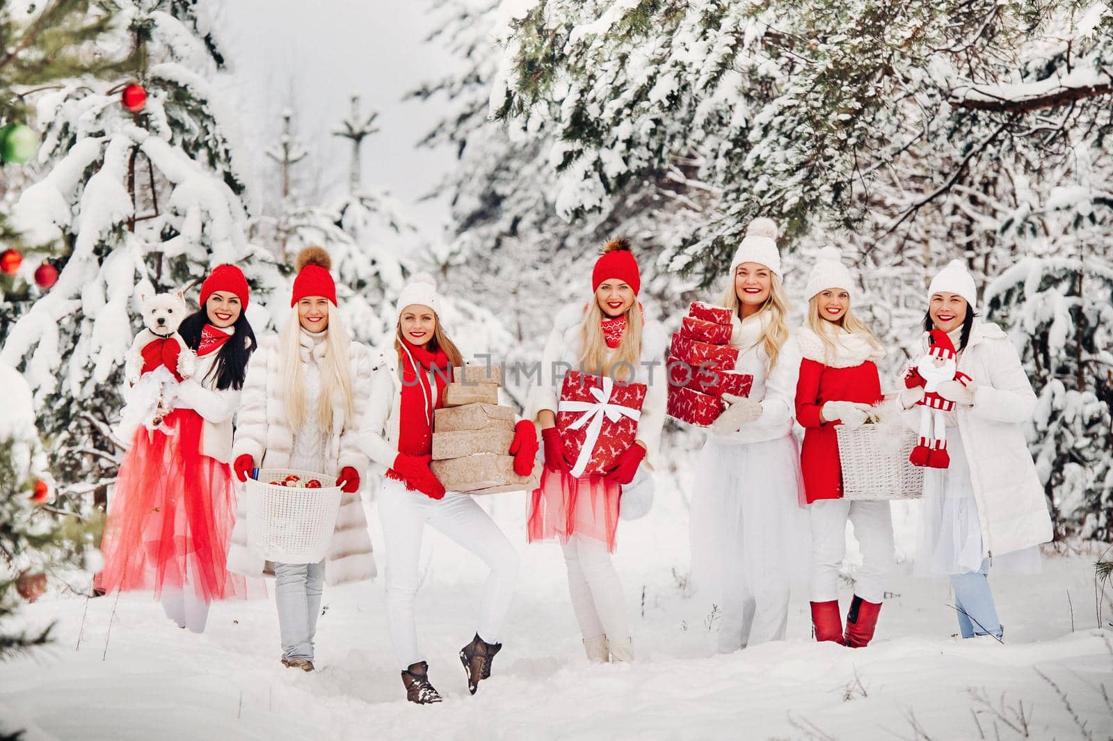 A large group of girls with Christmas gifts in their hands standing in the winter forest.Girls in red and white clothes with Christmas gifts in the snowy forest.