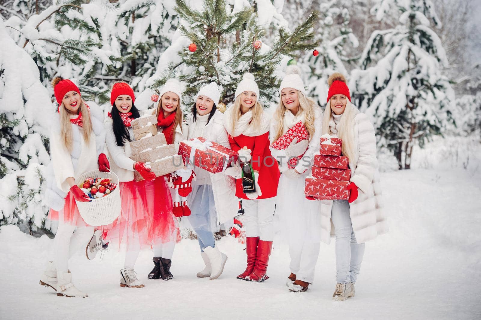 A large group of girls with Christmas gifts in their hands standing in the winter forest.Girls in red and white clothes with Christmas gifts in the snowy forest.