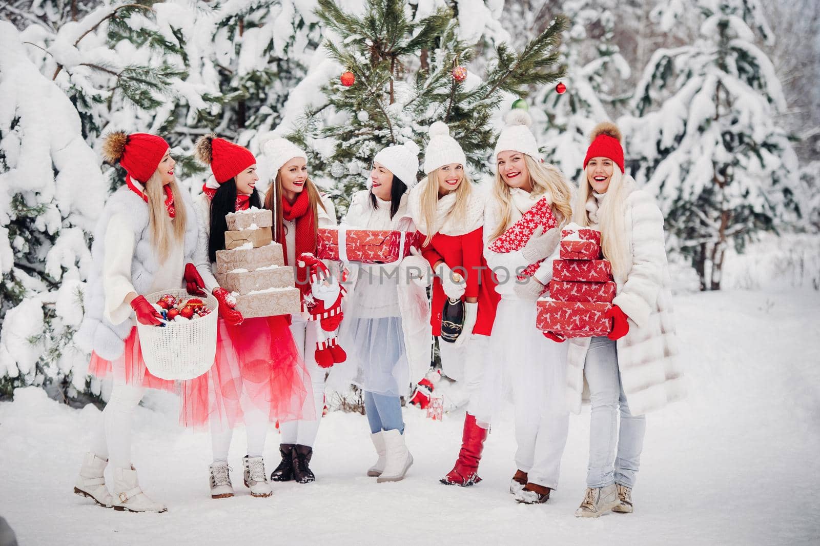 A large group of girls with Christmas gifts in their hands standing in the winter forest.Girls in red and white clothes with Christmas gifts in the snowy forest.