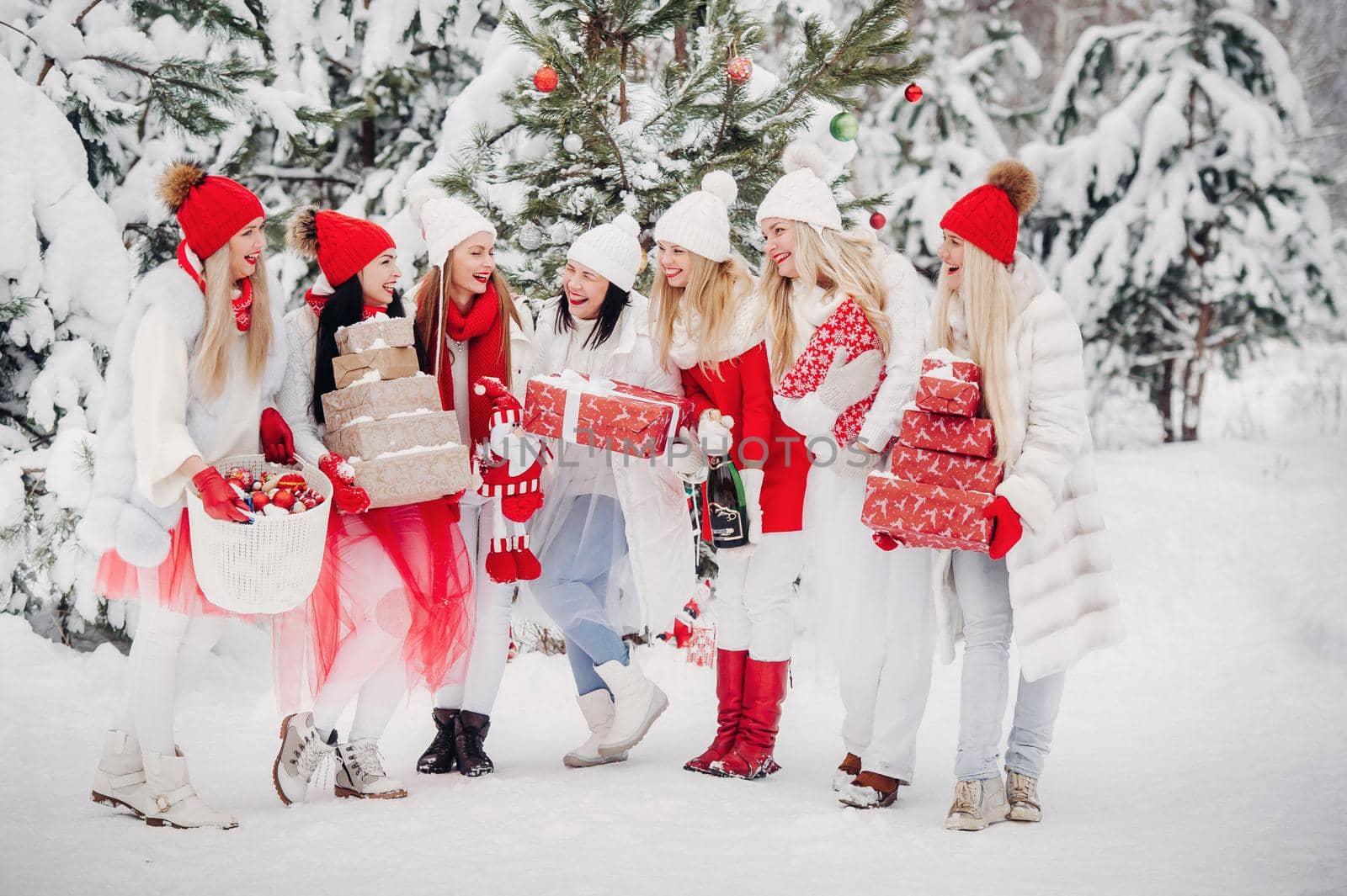 A large group of girls with Christmas gifts in their hands standing in the winter forest.Girls in red and white clothes with Christmas gifts in the snowy forest.