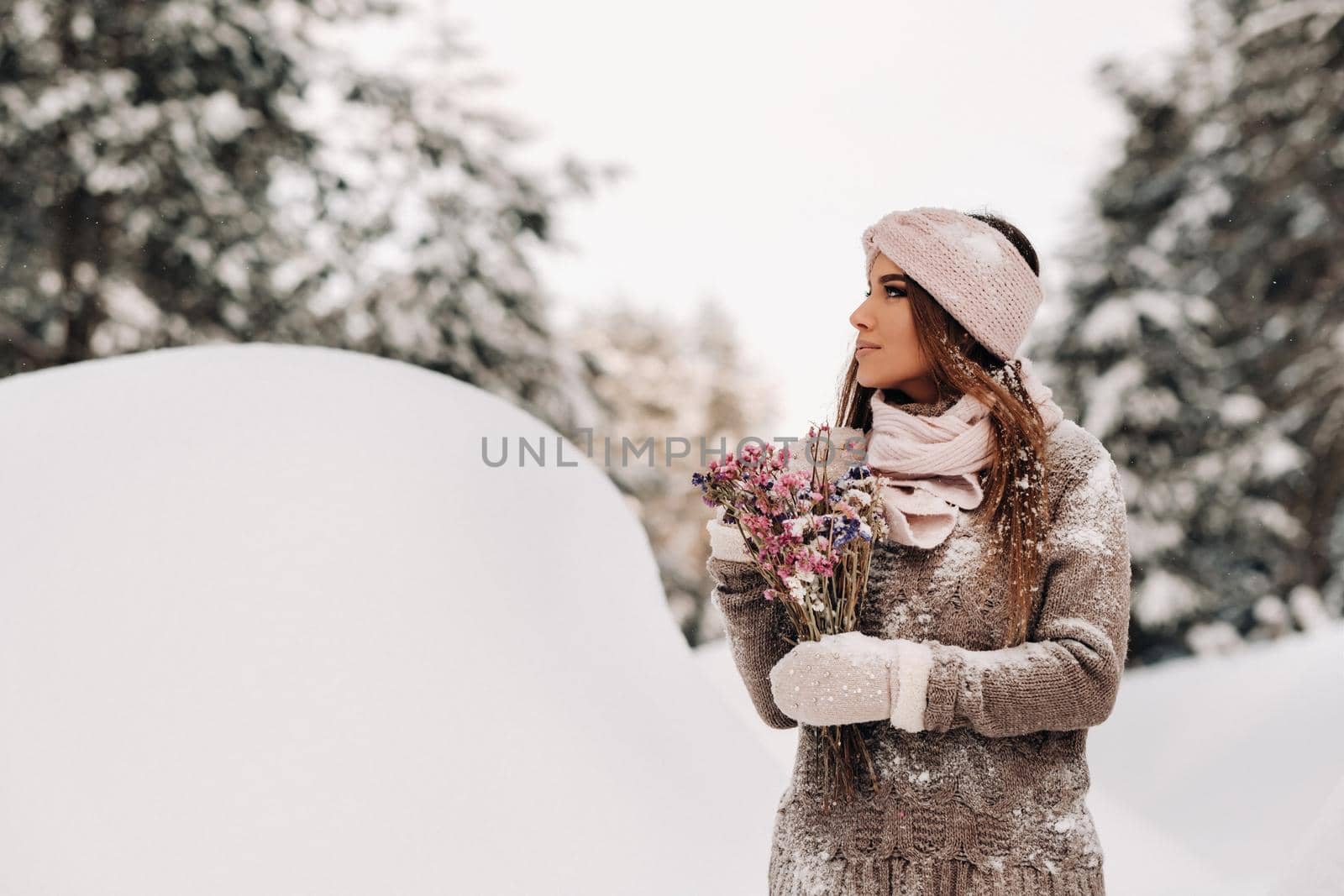 A girl in a sweater in winter with a bouquet in her hands stands among large snowdrifts.