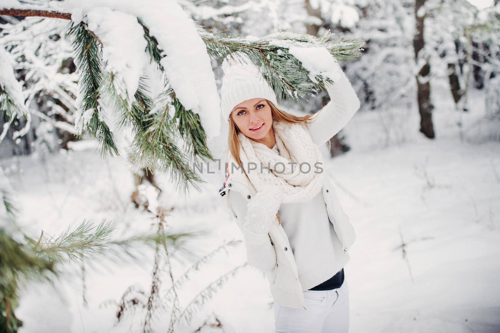 Portrait of a woman in white clothes in a cold winter forest. A girl with a white hat on her head in a snow-covered winter forest.