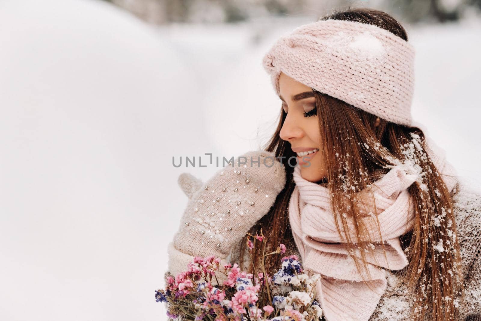 A girl in a sweater in winter with a bouquet in her hands stands among large snowdrifts.