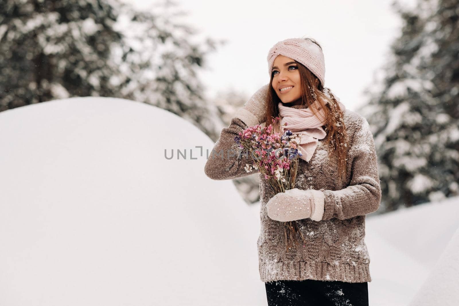 A girl in a sweater in winter with a bouquet in her hands stands among large snowdrifts.