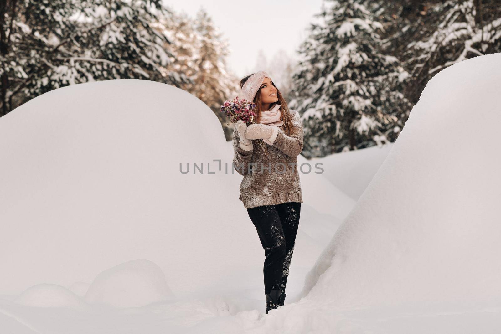 A girl in a sweater in winter with a bouquet in her hands stands among large snowdrifts.