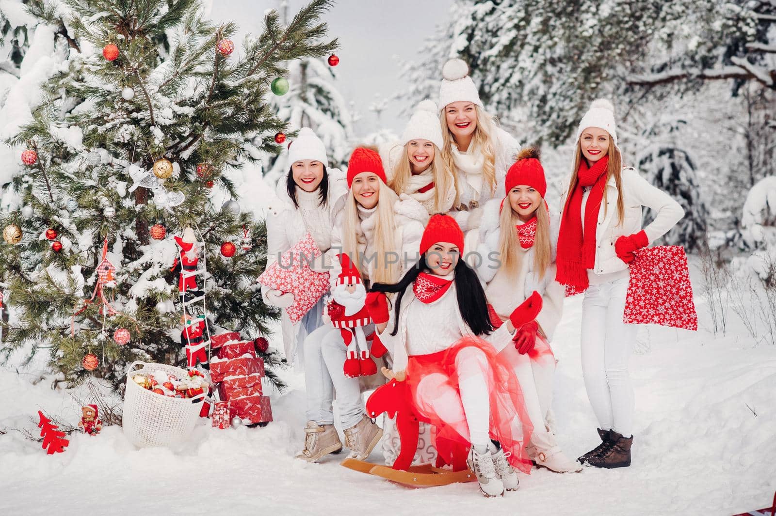 A large group of girls with Christmas gifts in their hands standing in the winter forest.Girls in red and white clothes with Christmas gifts in the snowy forest.