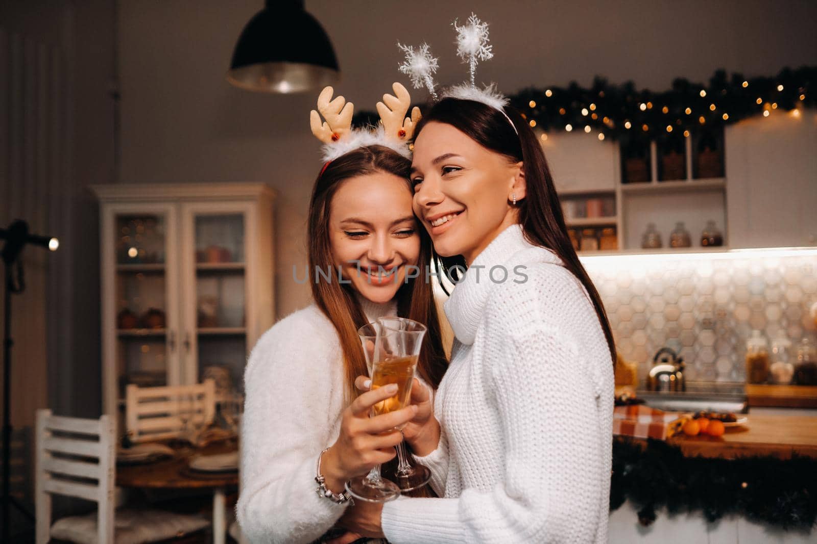 two girls in a cozy home environment with champagne in their hands at Christmas. Smiling girls drink champagne on a festive evening.