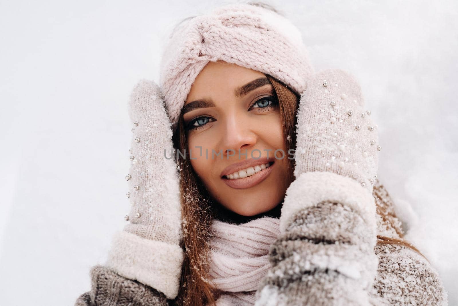 A girl in a sweater and mittens in winter stands on a snow-covered background.