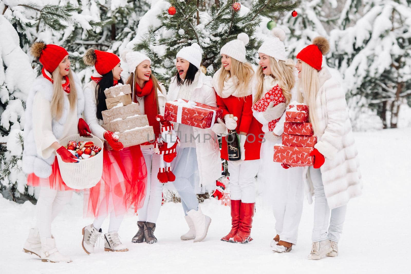 A large group of girls with glasses of champagne in their hands stands in the winter forest.Girls in red and white clothes with new year's drinks in a snow-covered forest