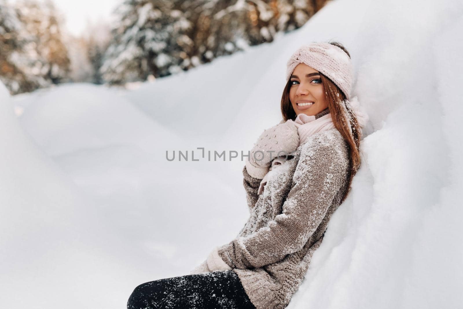 A girl in a sweater and mittens in winter stands on a snow-covered background.