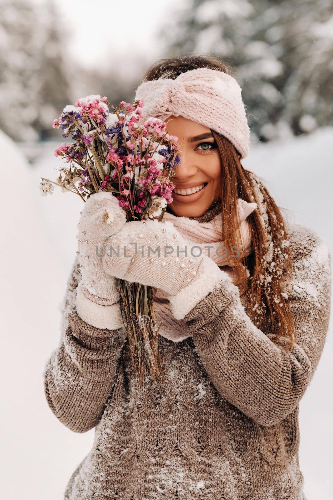 A girl in a sweater in winter with a bouquet in her hands stands among large snowdrifts.