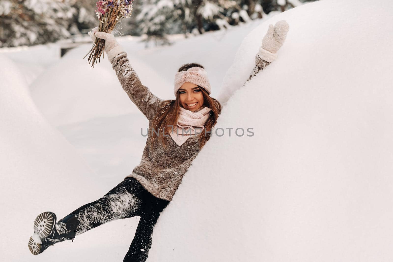 A girl in a sweater in winter with a bouquet in her hands stands among large snowdrifts.