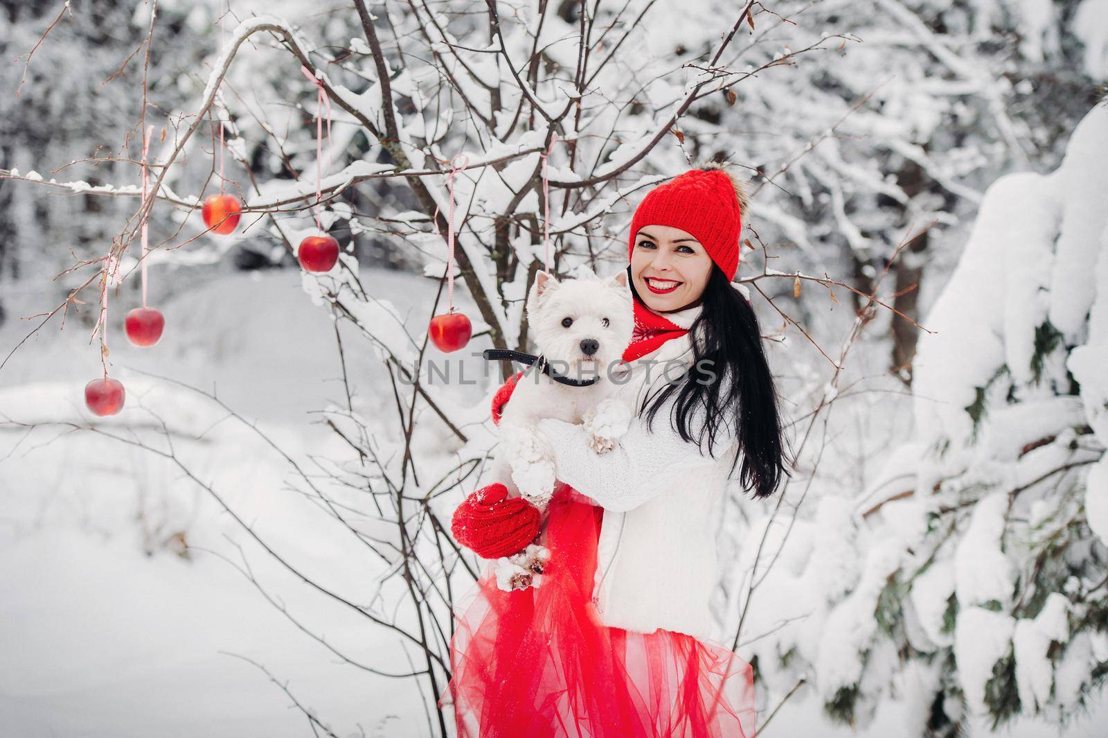 Portrait of a woman in a red jacket with a dog in a cold winter forest. A girl holds a dog in her hands in a snow-covered winter forest.