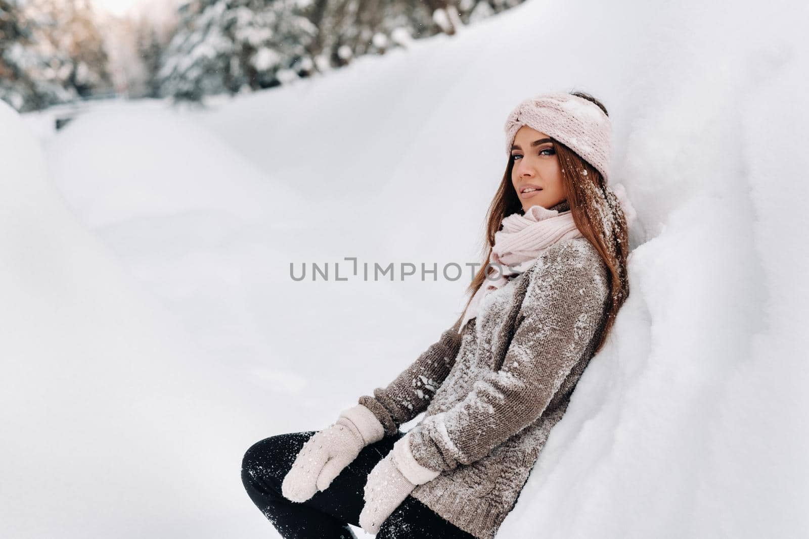 A girl in a sweater and mittens in winter stands on a snow-covered background.