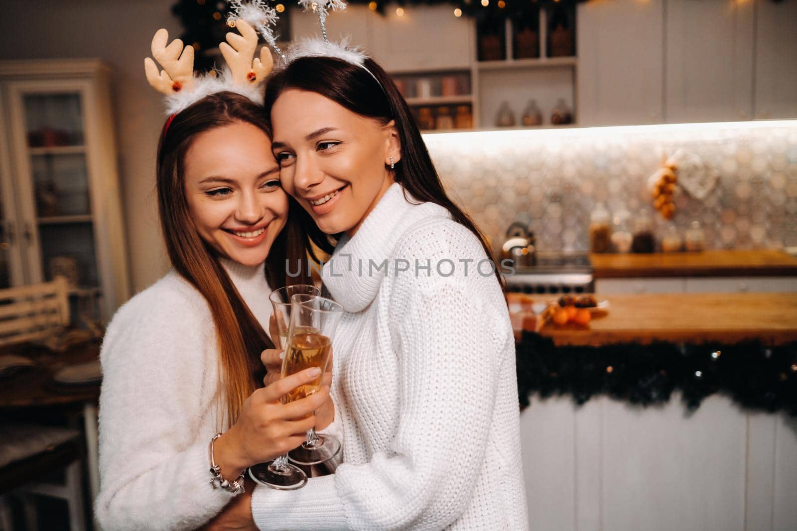two girls in a cozy home environment with champagne in their hands at Christmas. Smiling girls drink champagne on a festive evening by Lobachad