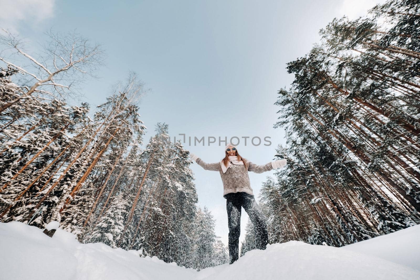 A girl in a sweater and mittens in winter stands on a snow-covered background.