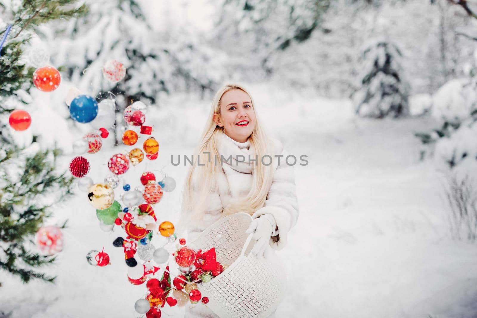 A girl in a white jacket throws Christmas balls to decorate the Christmas tree.A girl throws Christmas decorations from a basket into the winter forest.