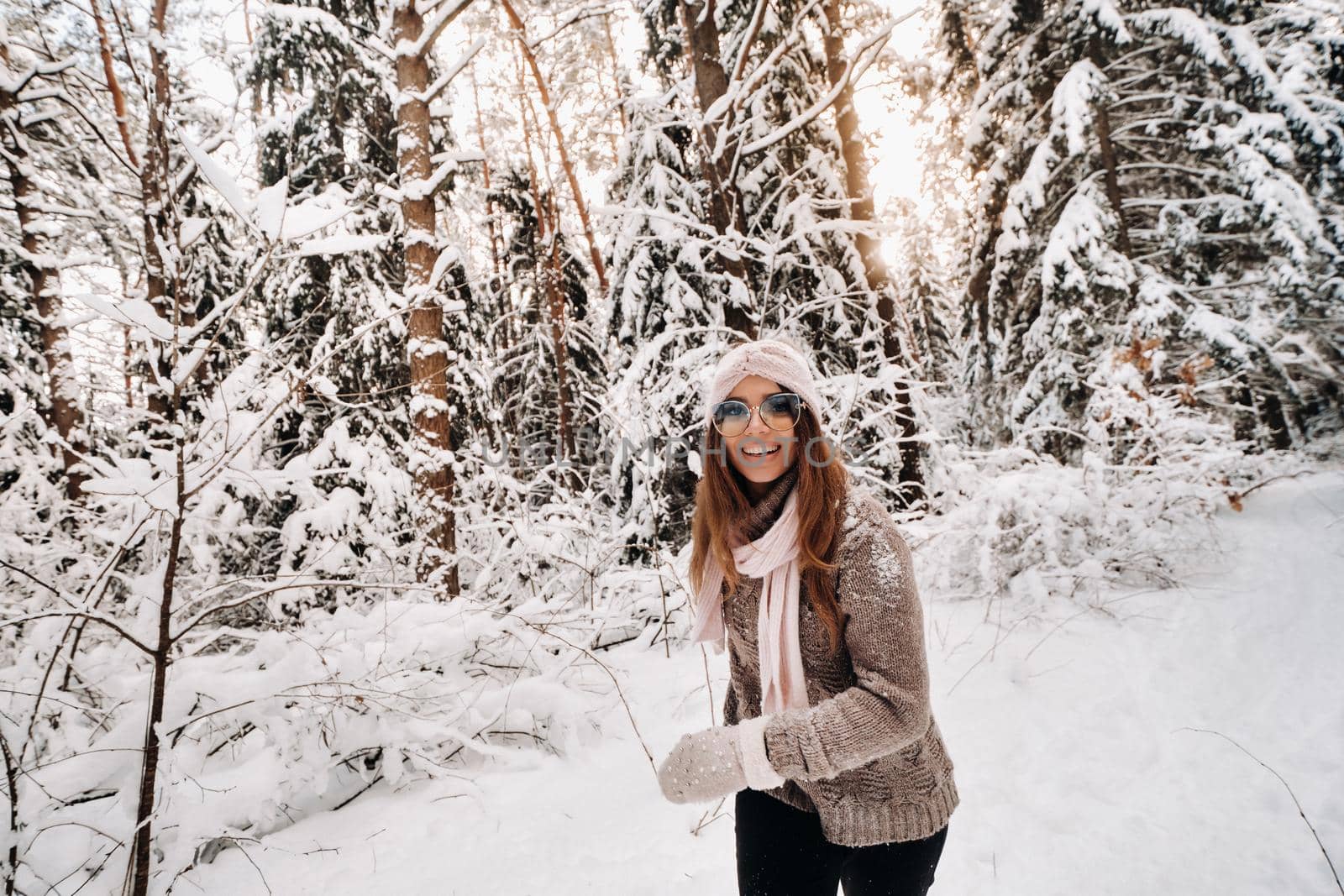 A girl in a sweater and glasses walks in the snow-covered forest in winter.
