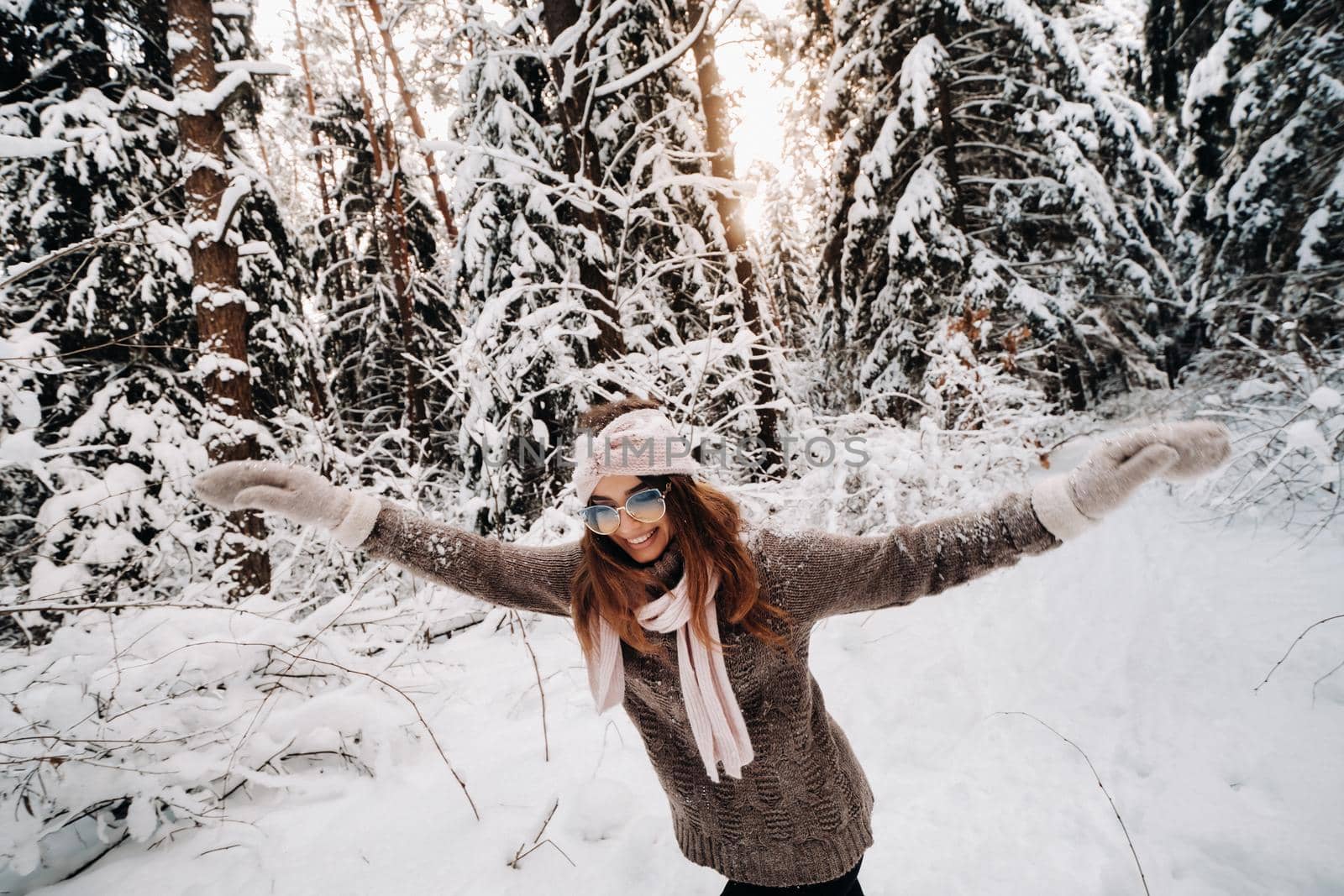 A girl in a sweater and glasses walks in the snow-covered forest in winter.