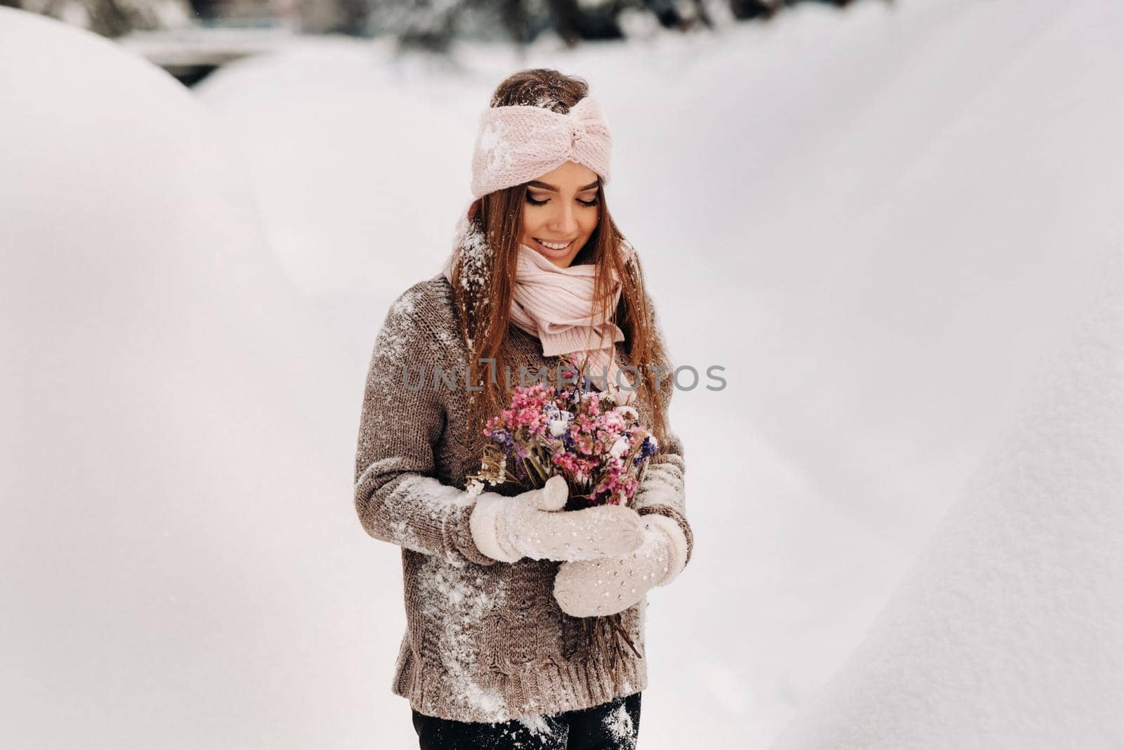 A girl in a sweater in winter with a bouquet in her hands stands among large snowdrifts.