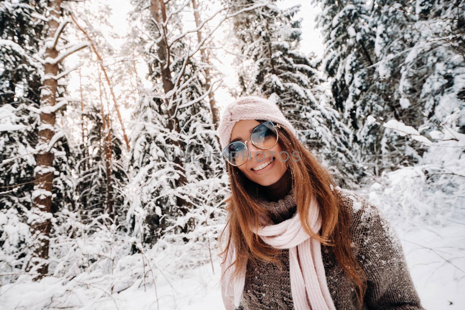 A girl in a sweater and glasses in winter in a snow-covered forest.