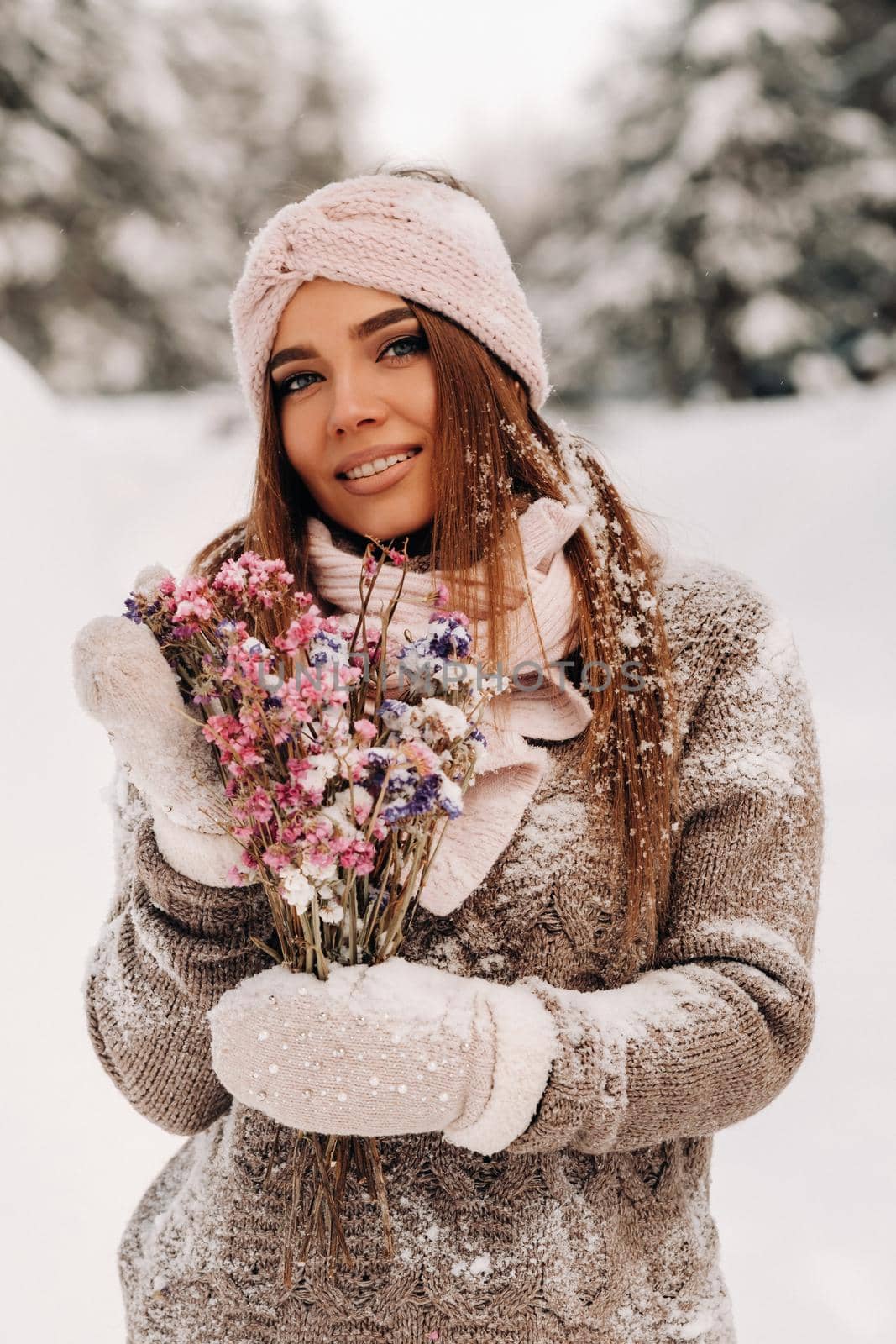 A girl in a sweater in winter with a bouquet in her hands stands among large snowdrifts.