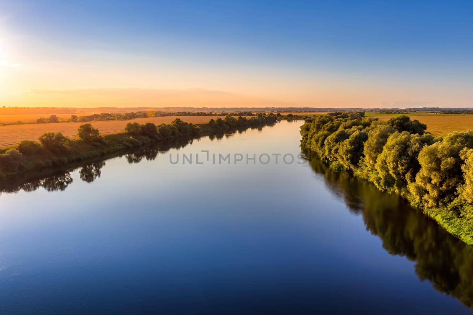 A sunset or sunrise scene over a lake or river with skies reflecting in the water on a summer evening or morning. Landscape.