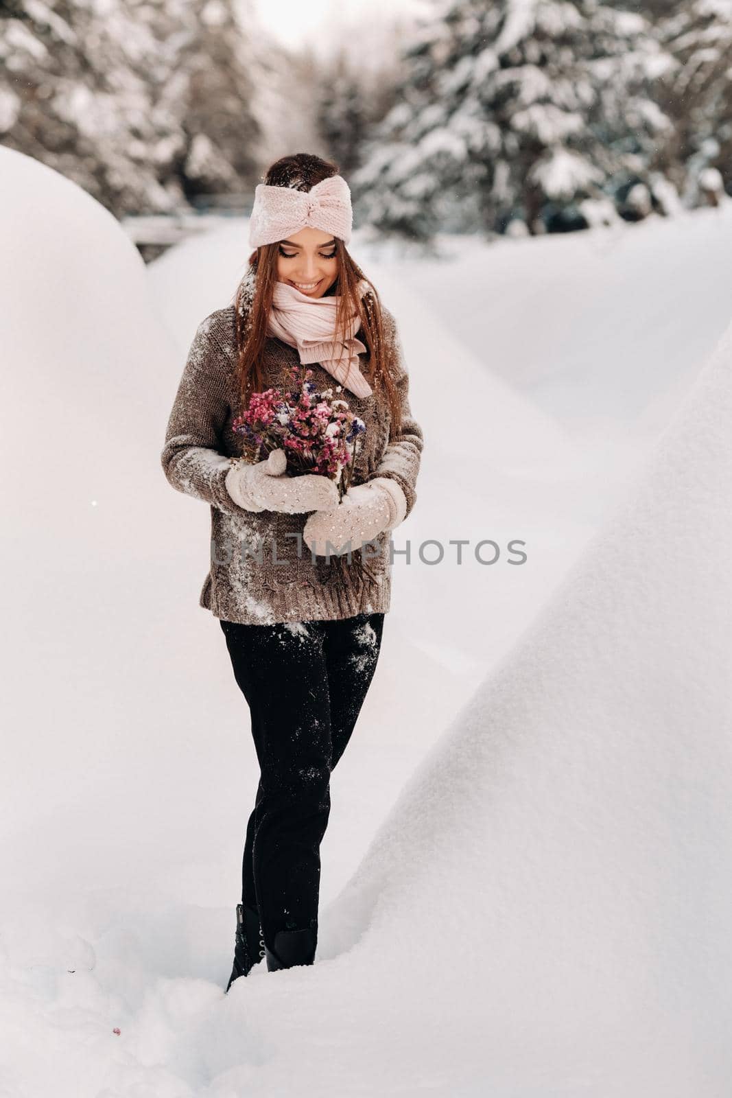 A girl in a sweater in winter with a bouquet in her hands stands among large snowdrifts by Lobachad