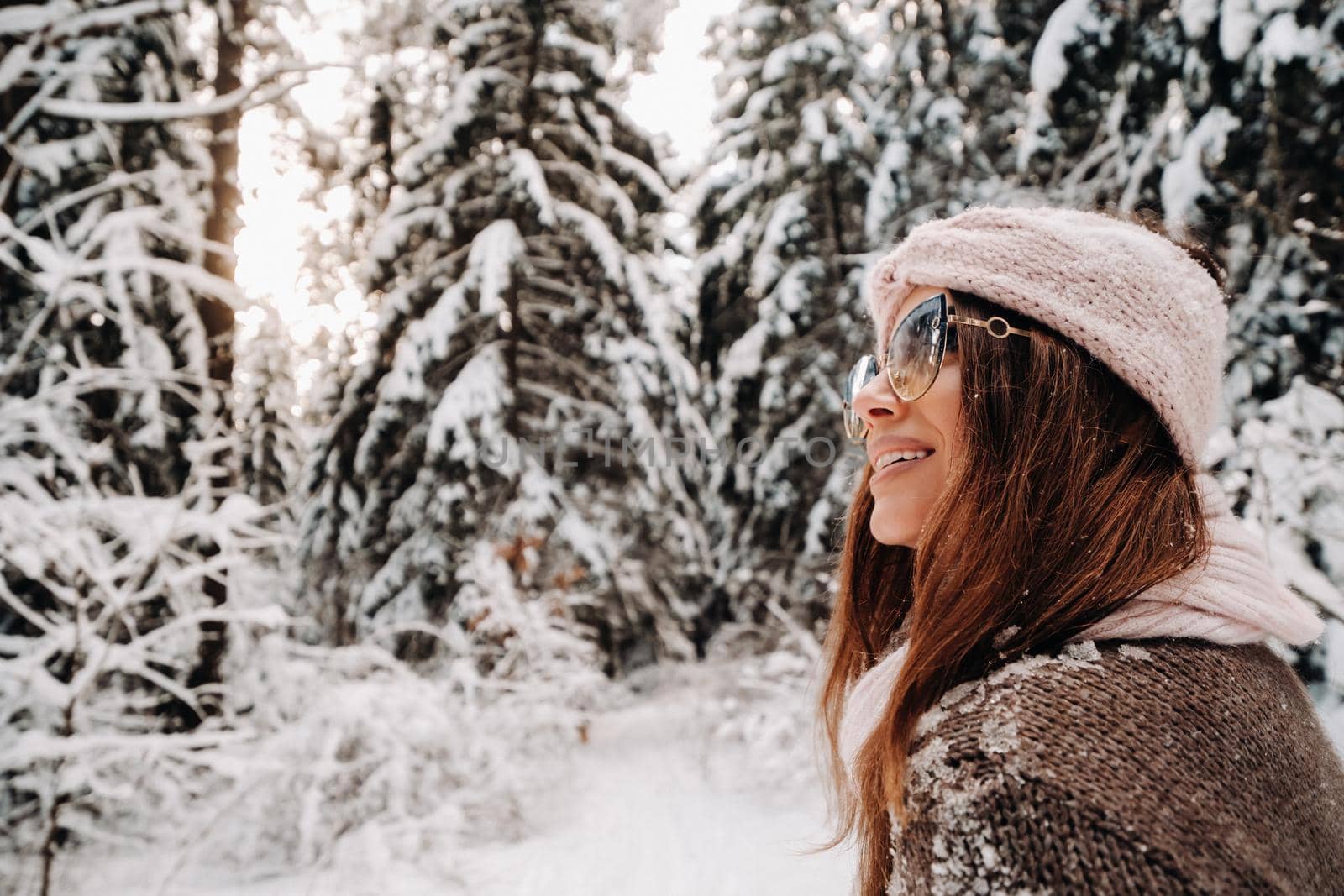 A girl in a sweater and glasses in winter in a snow-covered forest.