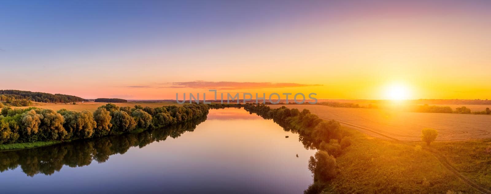 A sunset or sunrise scene over a lake or river with skies reflecting in the water on a summer evening or morning. Panorama.