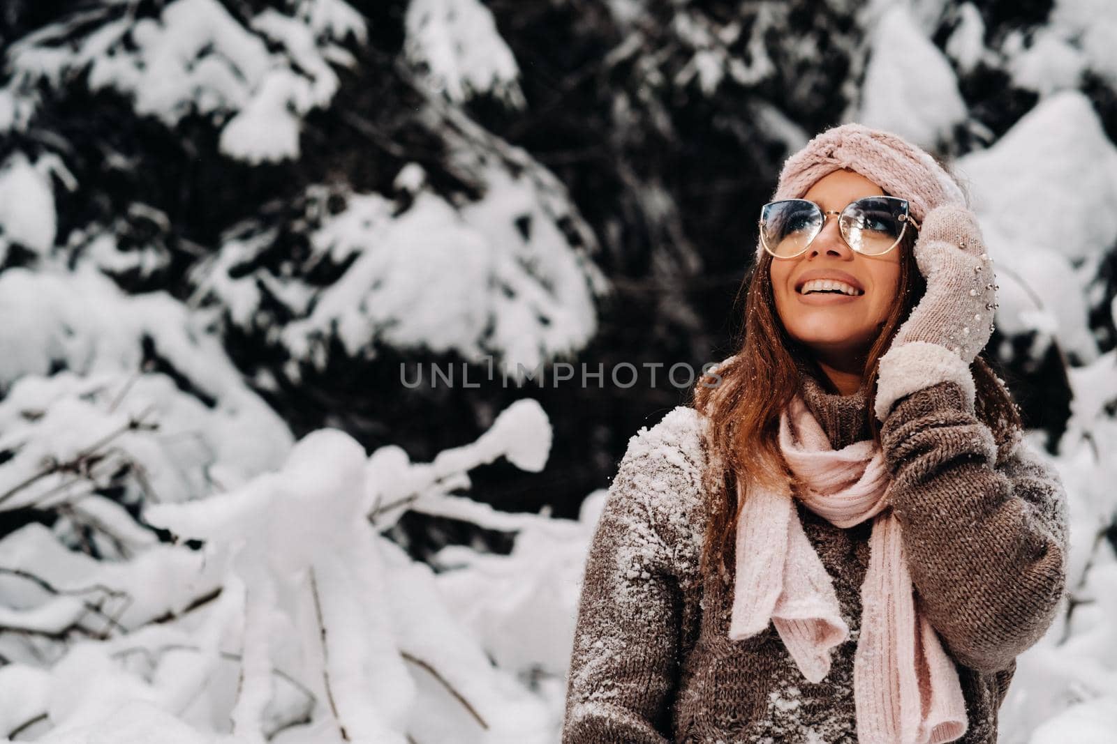 A girl in a sweater and glasses in winter in a snow-covered forest.