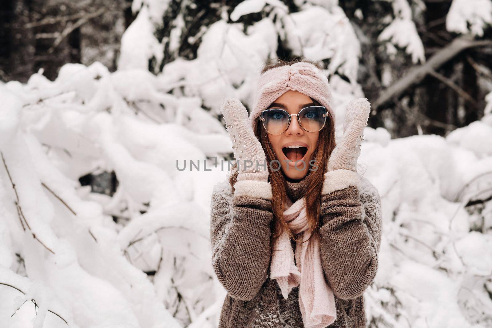 A girl in a sweater and mittens in winter holds her head with her hands in a snowy forest.
