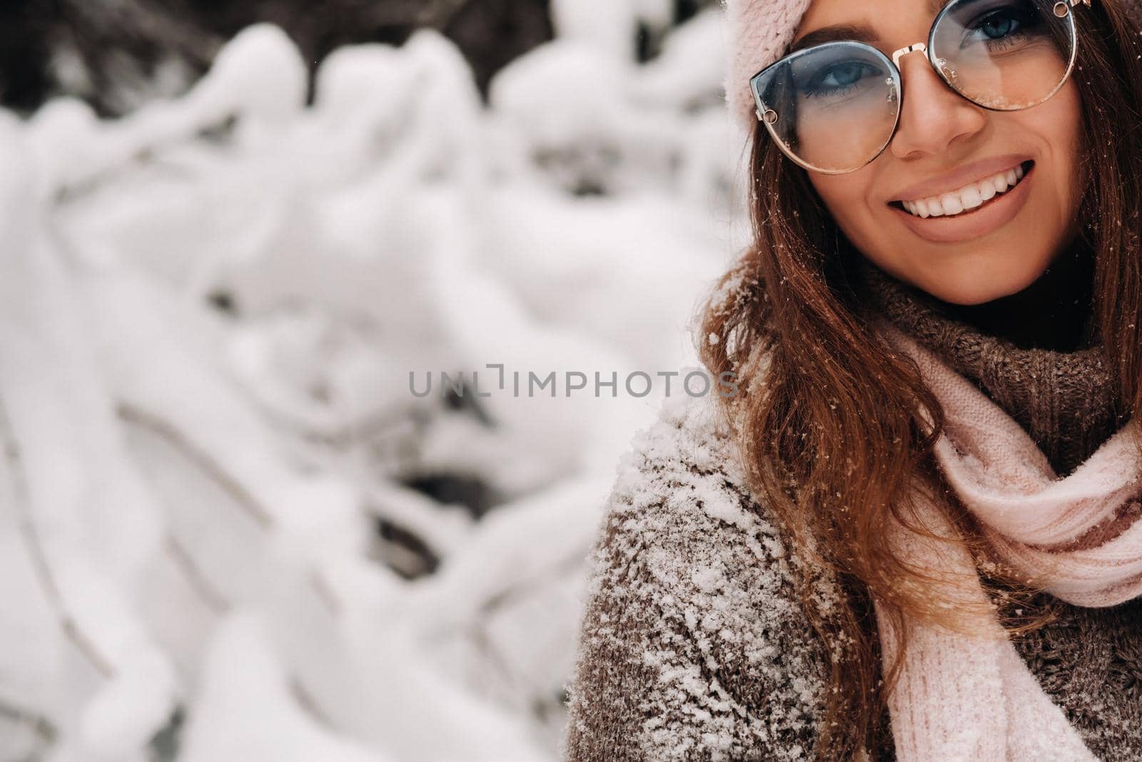 A girl in a sweater and glasses in winter in a snow-covered forest.