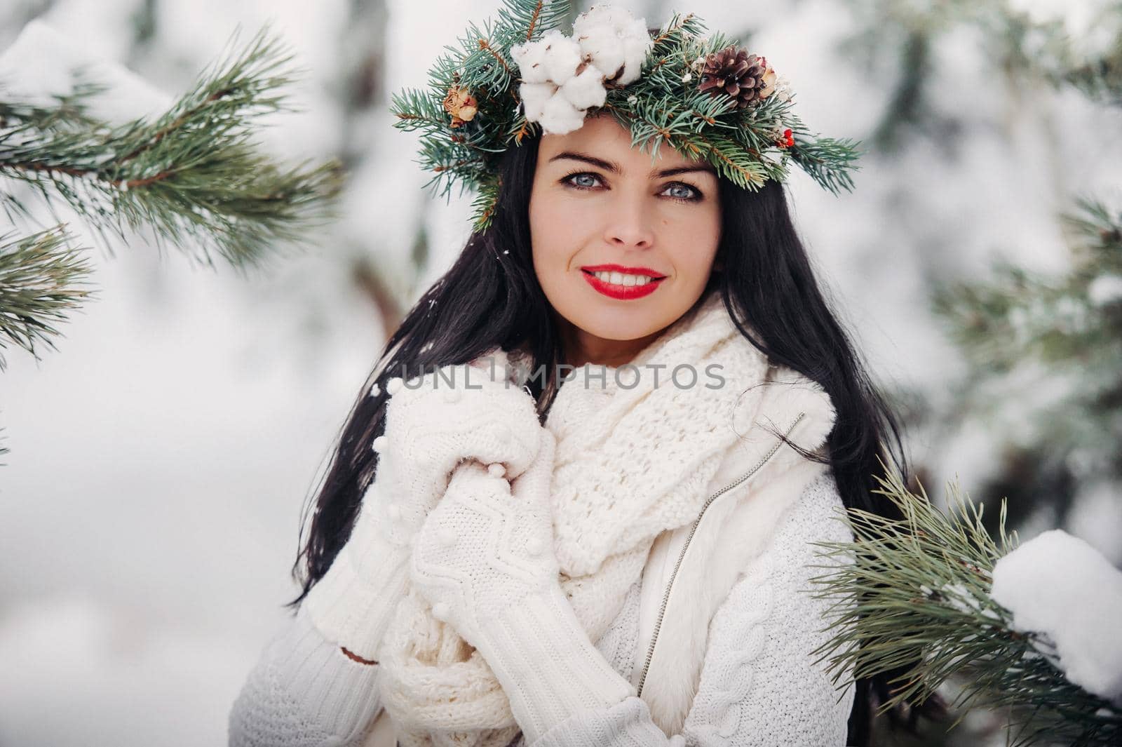 Portrait of a woman in white clothes in a cold winter forest. Girl with a wreath on her head in a snow-covered winter forest.