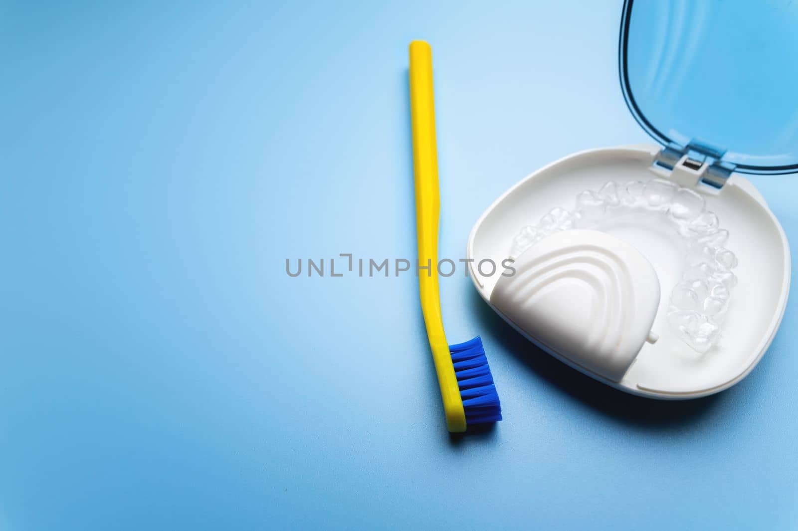 transparent braces in a special storage box with a toothbrush lie on a blue background, close-up. daily dental care concept by yanik88