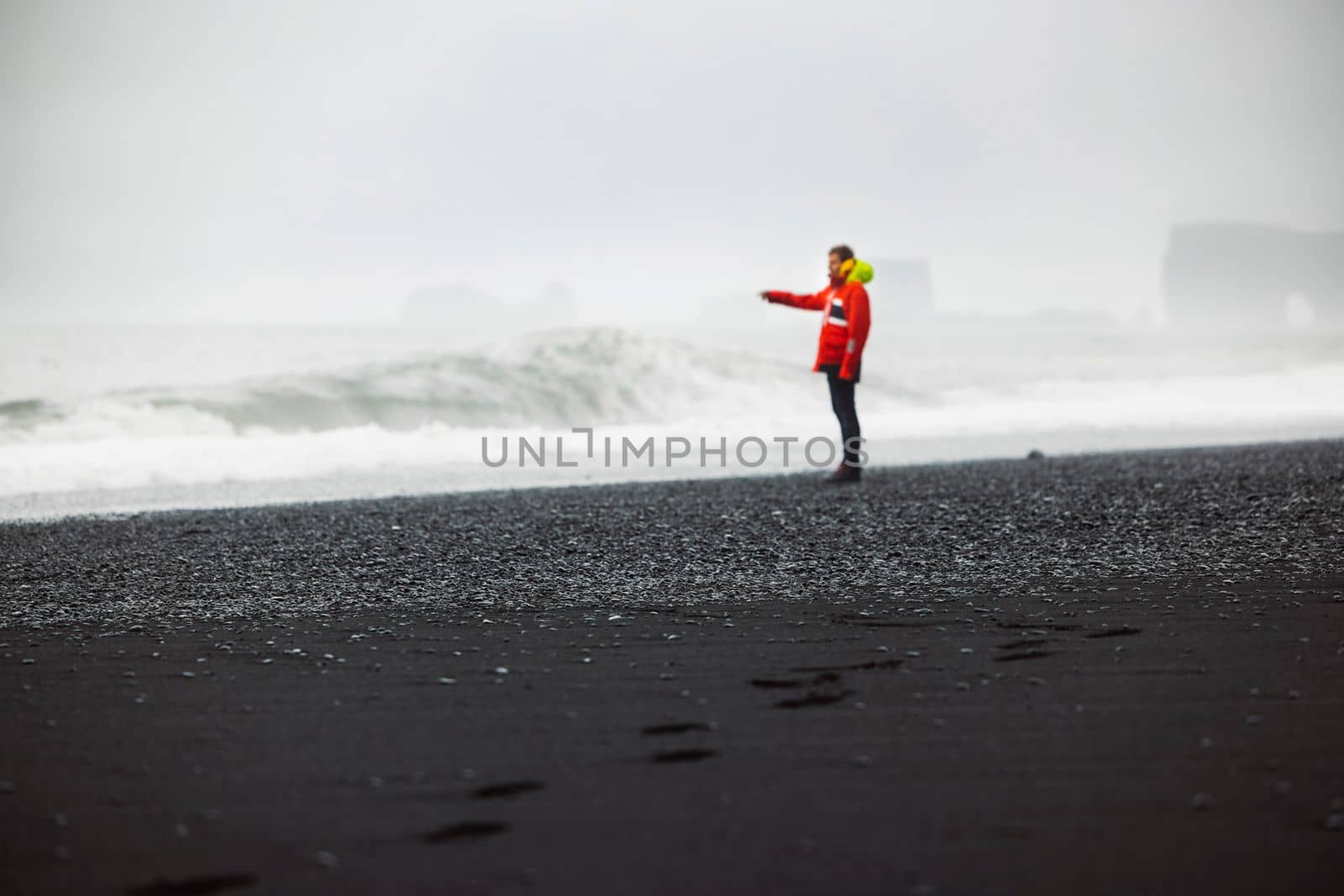 The man in waterproof jacket and pants standing on the beach with black volcanic sand, Reynisfjara, south of Iceland. Icelandic nature, Atlantic Ocean shore, seaside. High quality photo