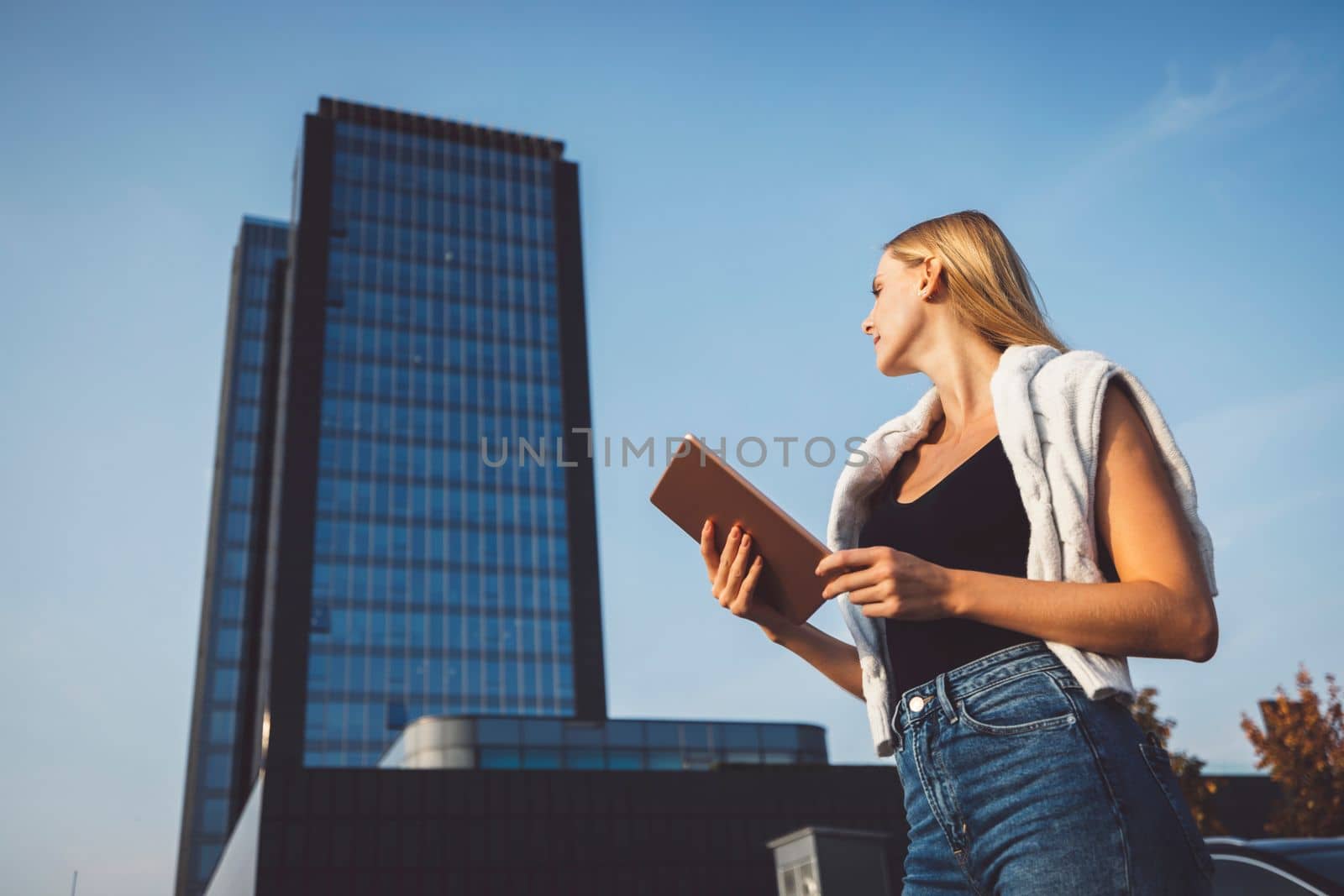 Low angle view of blonde woman holding a digital tablet with skyscraper in the background by VisualProductions