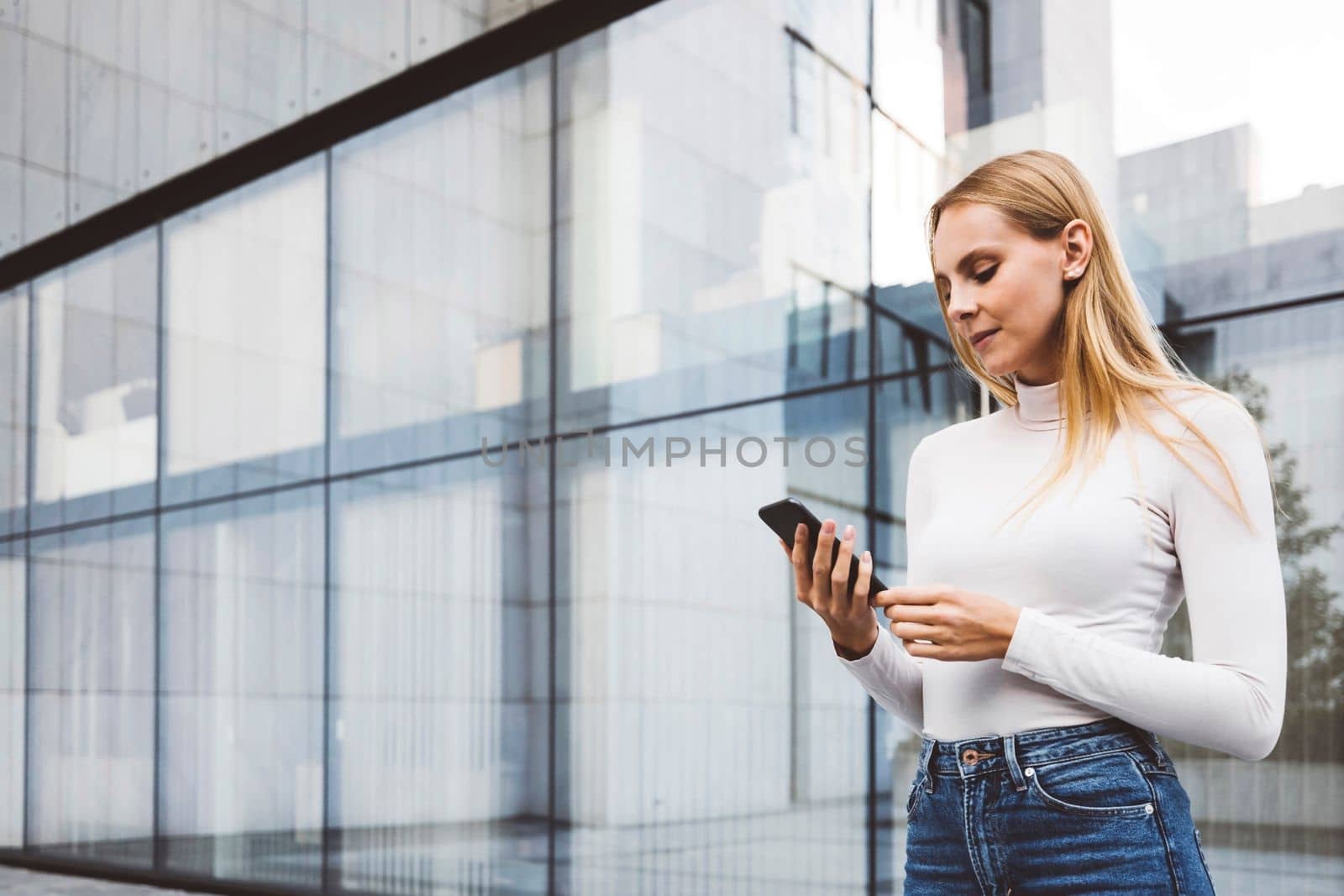 Waist up woman in urban setting standing outside looking at her phone by VisualProductions