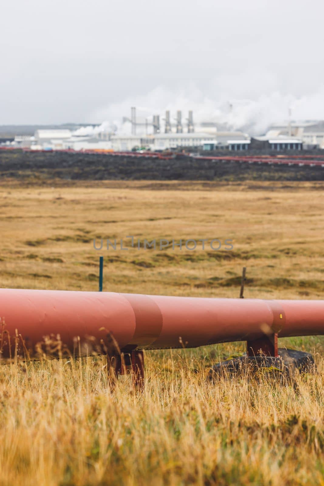 Geothermal Power Plant, hot water power station in Iceland. Steam rolling out of the plant chimneys, red large tubes running across the grounds filled with hot water. Sustainable, energy efficient Cloudy cold autumn day in Iceland.