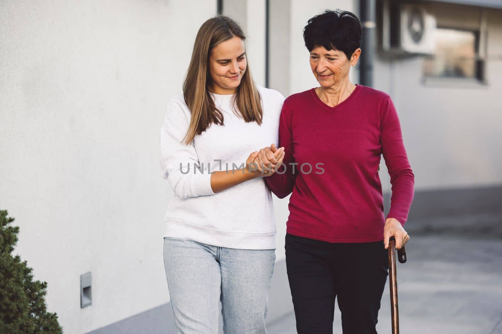 Young woman working as a home nurse taking care of a senior lady who is having trouble walking by VisualProductions