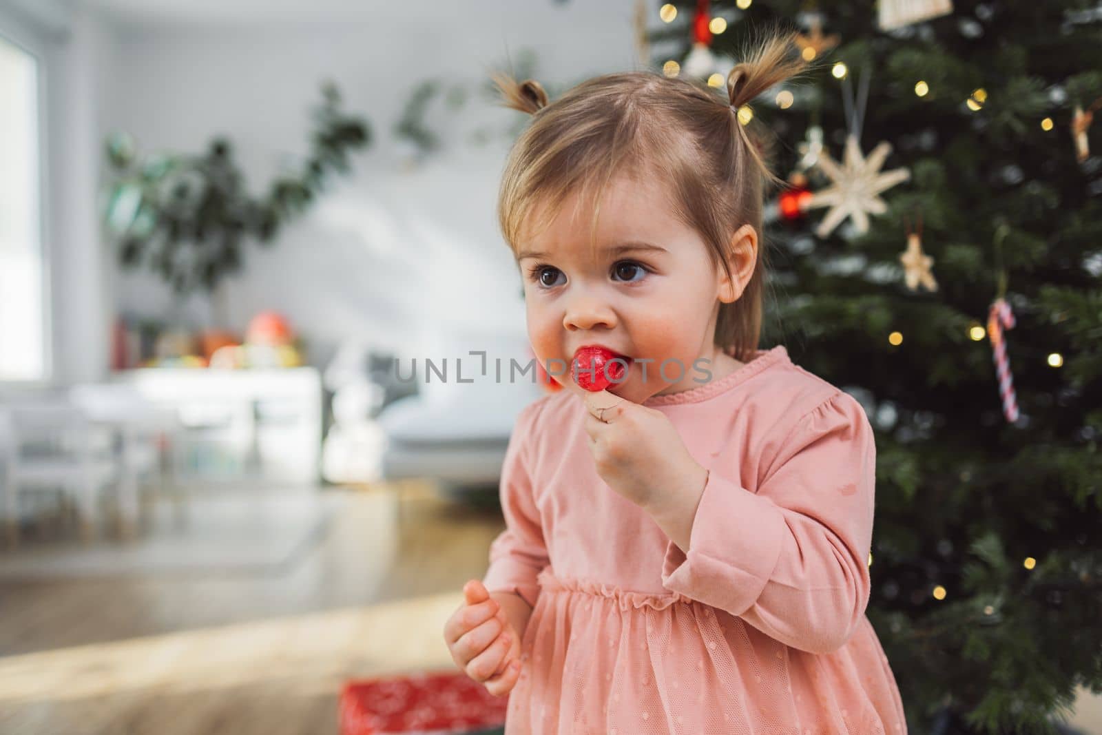 Cute little girl with two pony tails and a lollipop in her mouth wearing a beautiful pink dress by VisualProductions