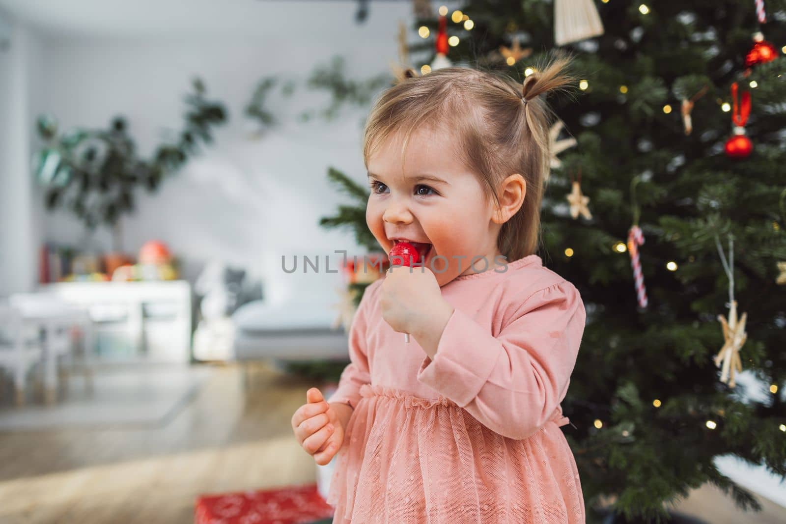 Smiling baby girl enjoys licking her lollipop on Christmas day by VisualProductions
