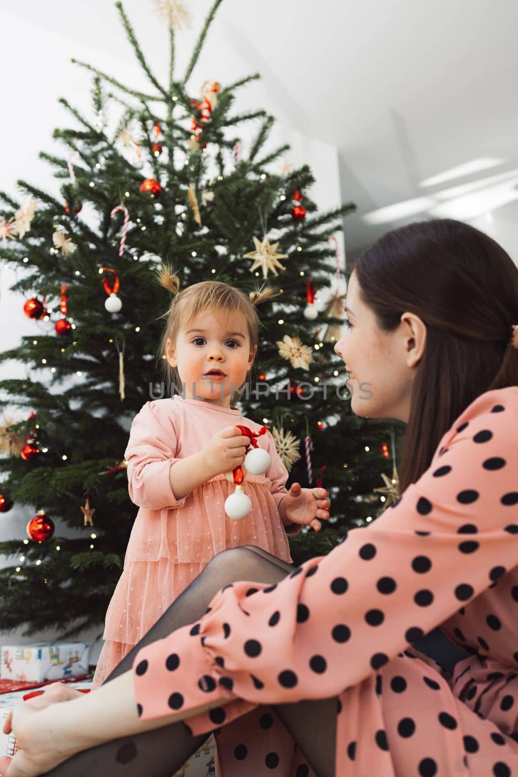 Vertical photo low angle view, of baby girl decorating the Christmas tree with mom by VisualProductions