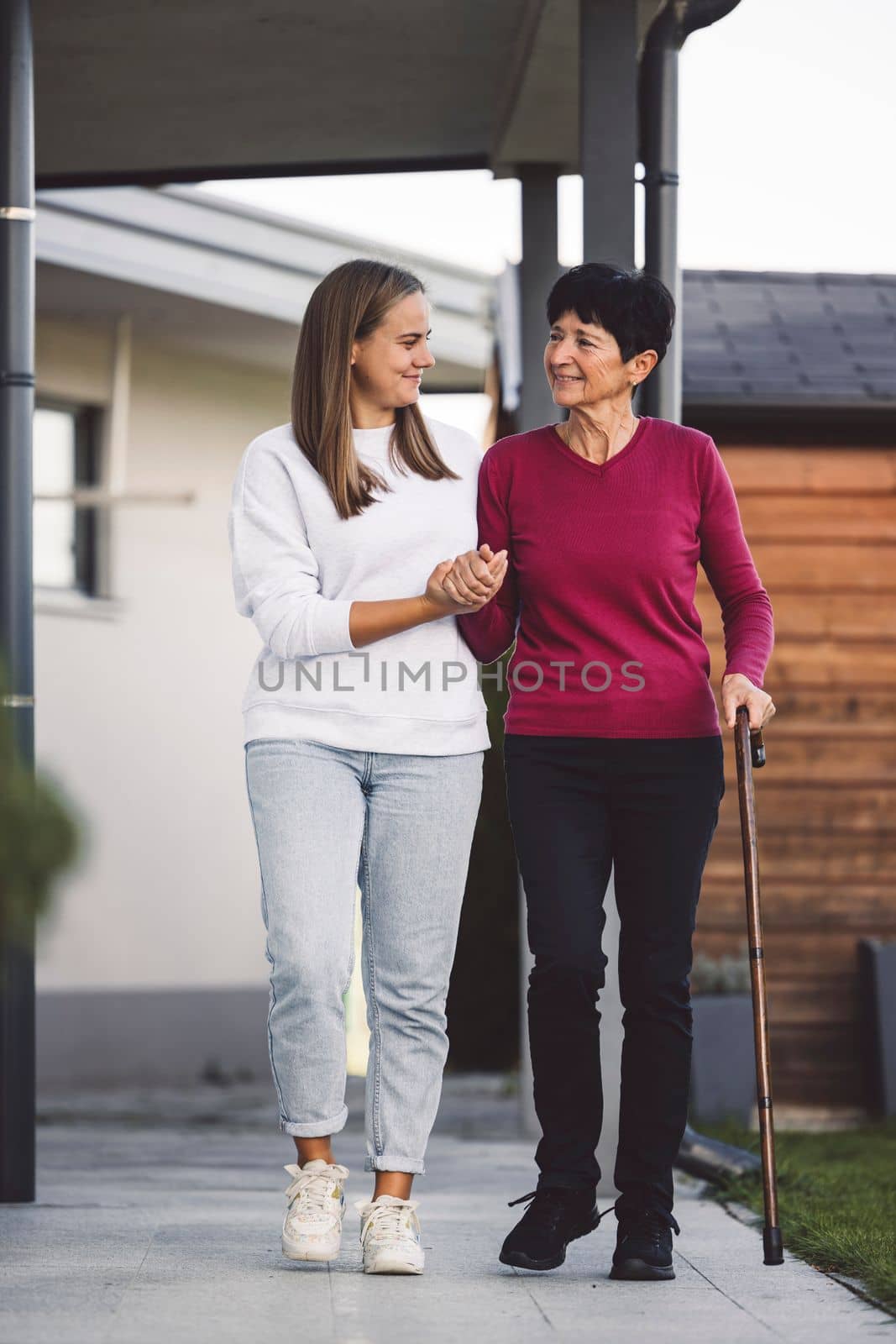 Young caucasian woman a nurse, on a home visit taking care of a senior lady. Nurse helping a senior women with every day chores, helping her to walk and move around the house.