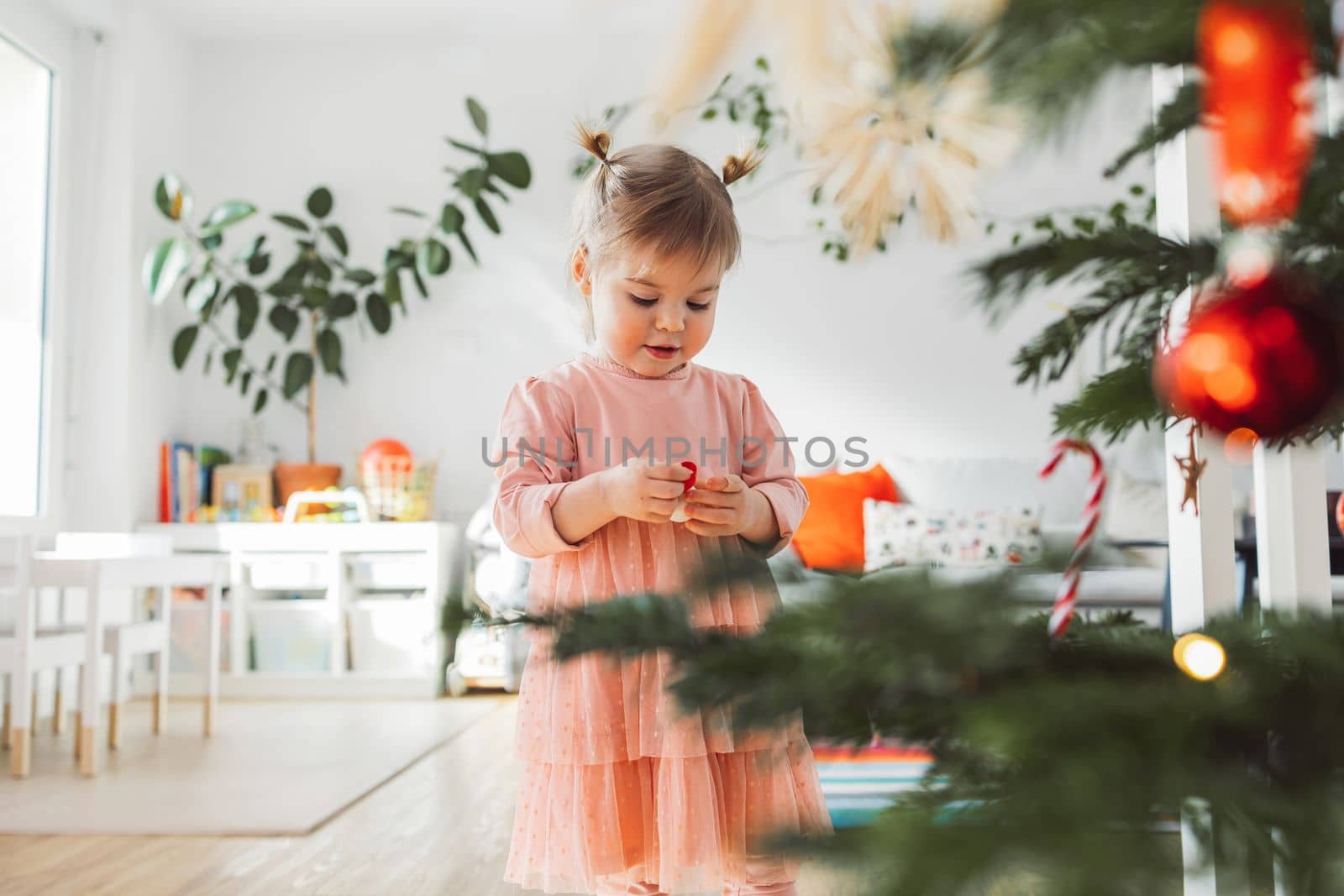 Beautiful caucasian baby gir with two little ponytails holding a Christmas ornament, looking at it with curiosity by VisualProductions