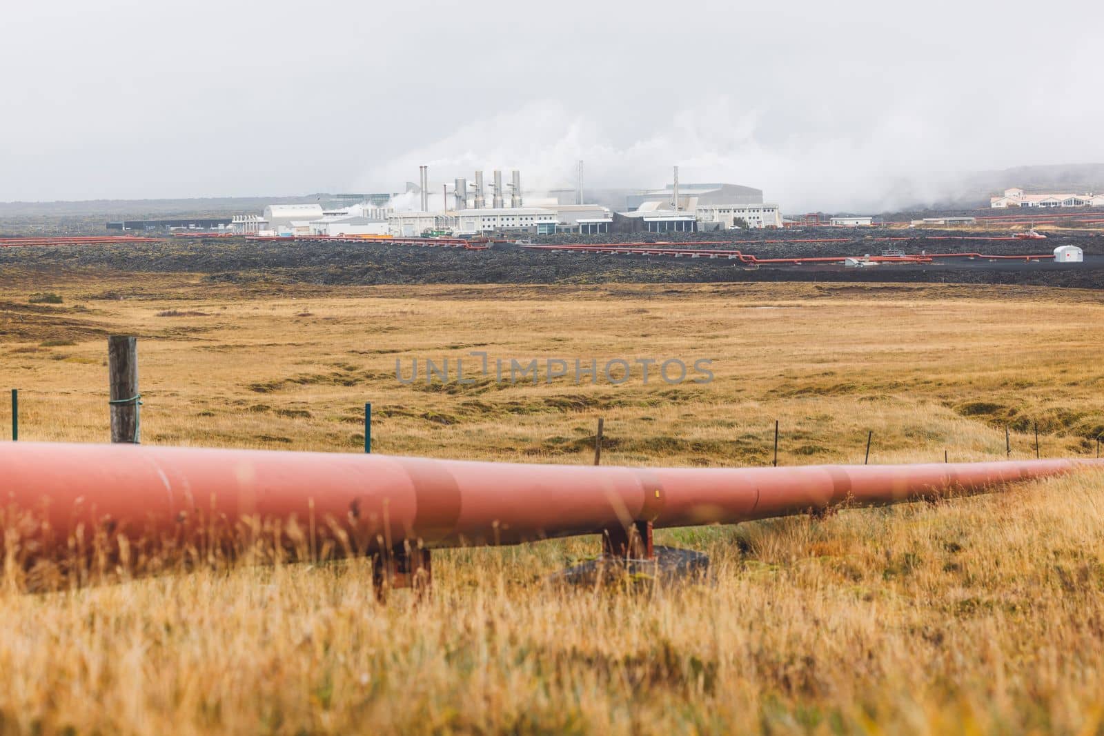 Geothermal Power Plant, hot water power station in Iceland. Steam rolling out of the plant chimneys, red large tubes running across the grounds filled with hot water. Sustainable, energy efficient Cloudy cold autumn day in Iceland.