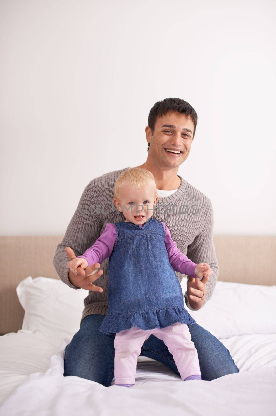 Dad and daughter- playful time together. A young father playing with his baby girl on the bed. by YuriArcurs