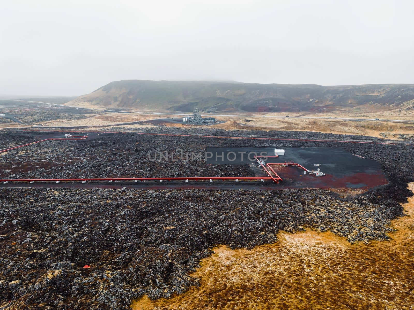 Geothermal Power Plant, hot water power station in Iceland. Steam rolling out of the plant chimneys, red large tubes running across the grounds filled with hot water. Sustainable, energy efficient Cloudy cold autumn day in Iceland.