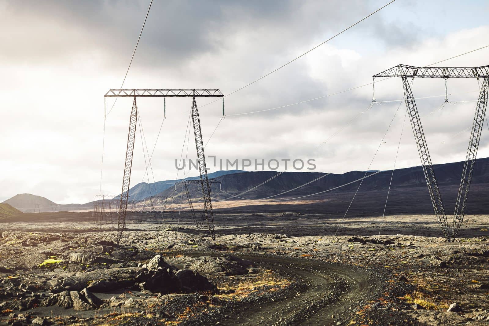 High voltage electrical cables on poles, with a backdrop of a cloudy sky. The lines are attached to the poles with glass insulation. The lines are running through the Icelandic highlands. High quality photo