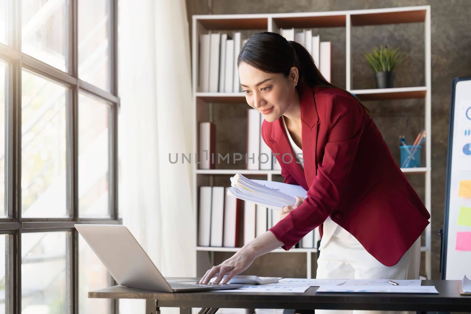 Smiling young woman looking at tablet working in office and .in hand holding business documents.
